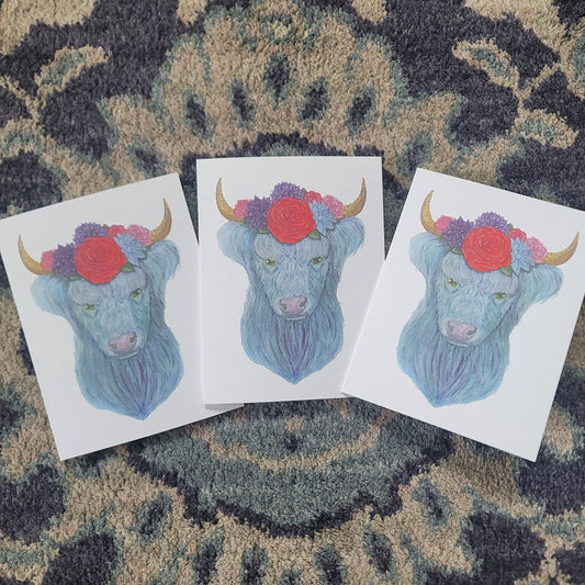 Three watercolor cards featuring a blue highland cow with flowers and horns on a patterned fabric background.