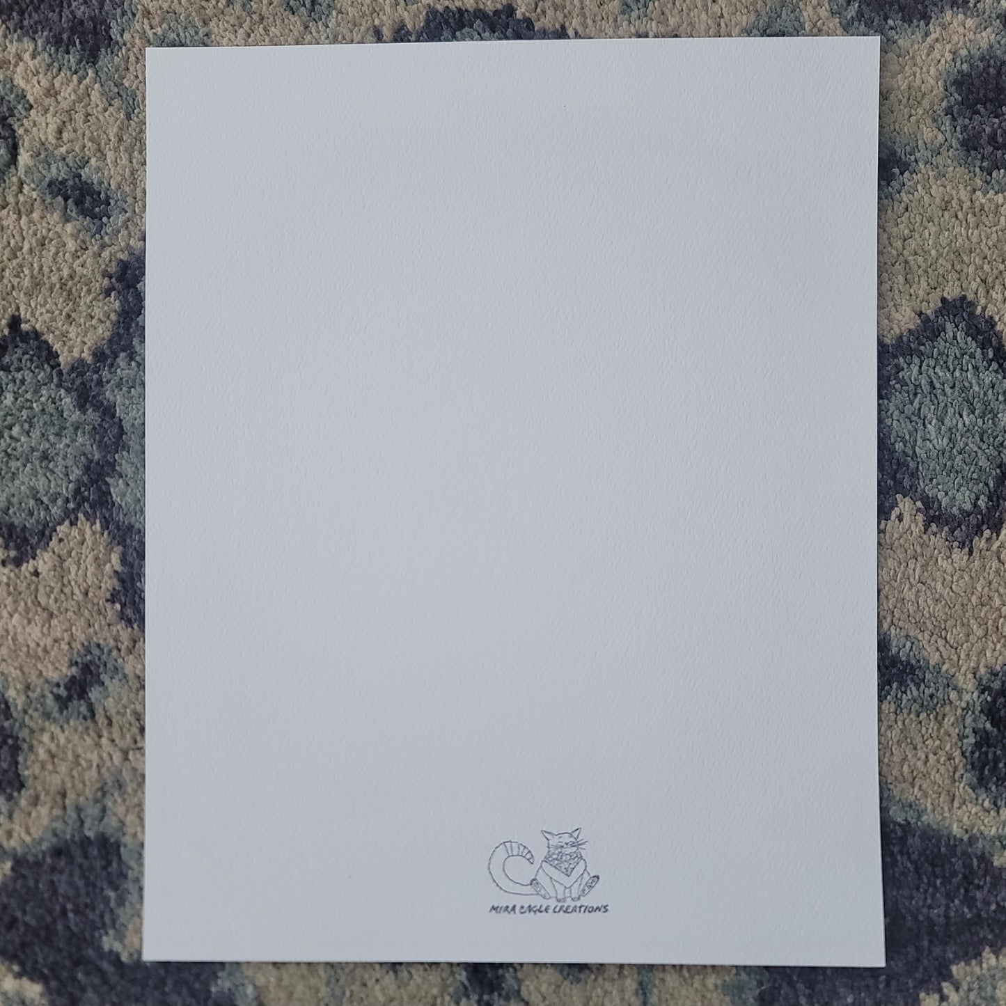 Blank white art print card with small gray logo at the bottom center on textured blue-gray surface.