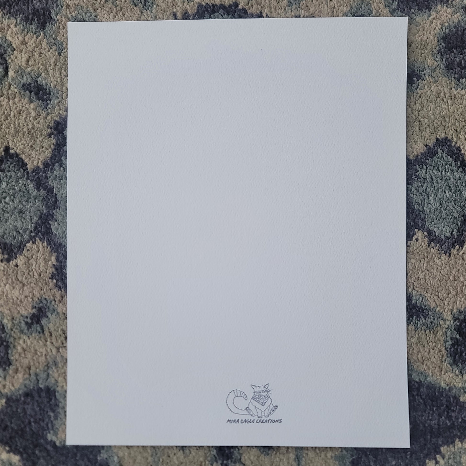 Blank white art print card with small gray logo at the bottom center on textured blue-gray surface.